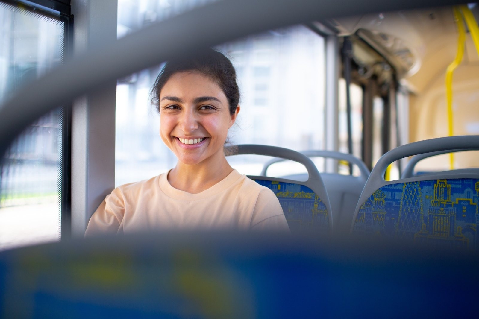 Smiling woman sitting on public transportation, seen between rows of blue seats.