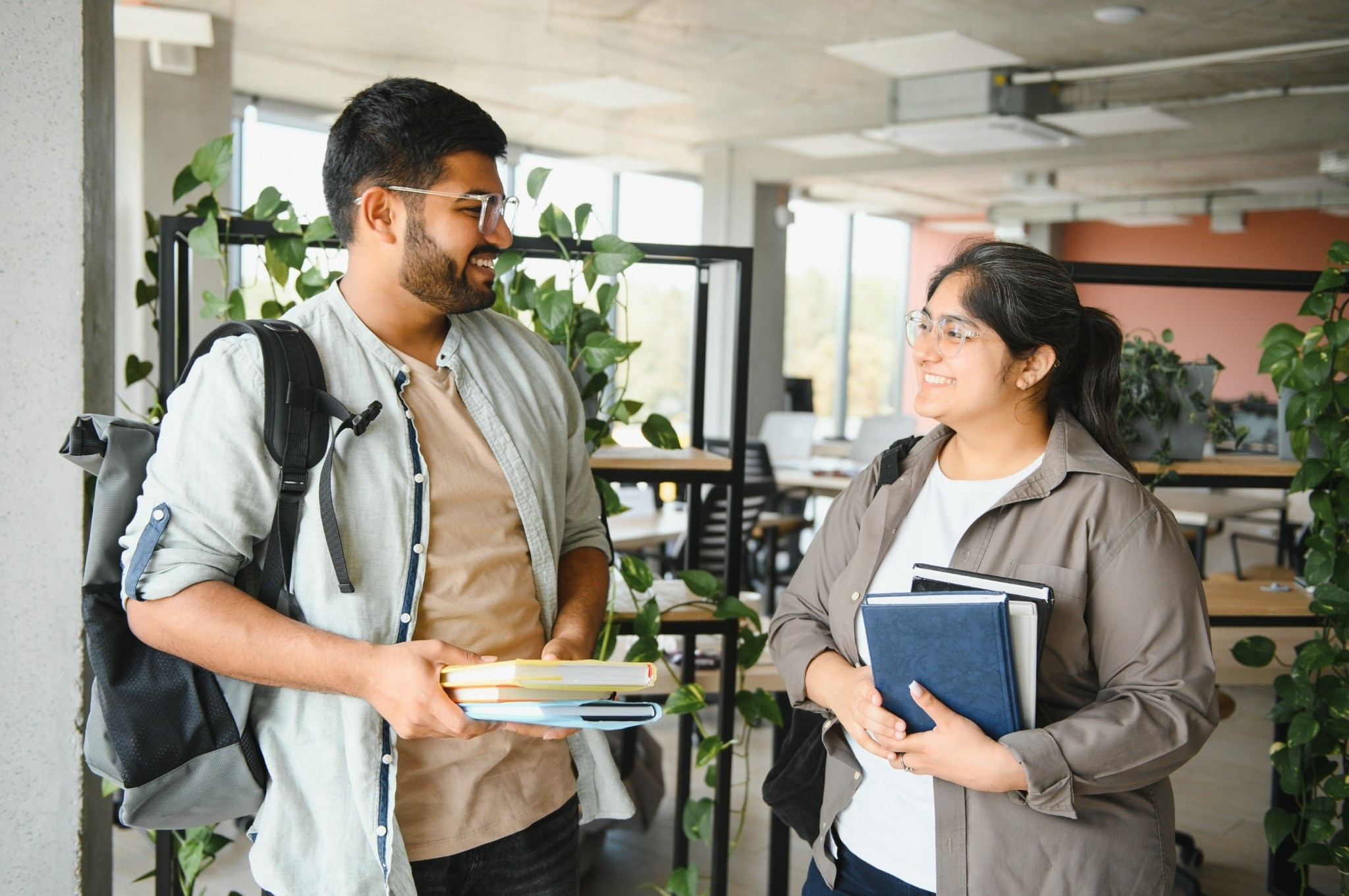 Two people holding books and talking in a bright indoor space