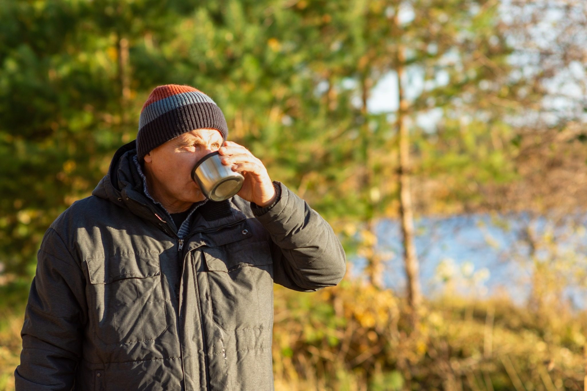 Man drinking from a metal cup outdoors near a lake