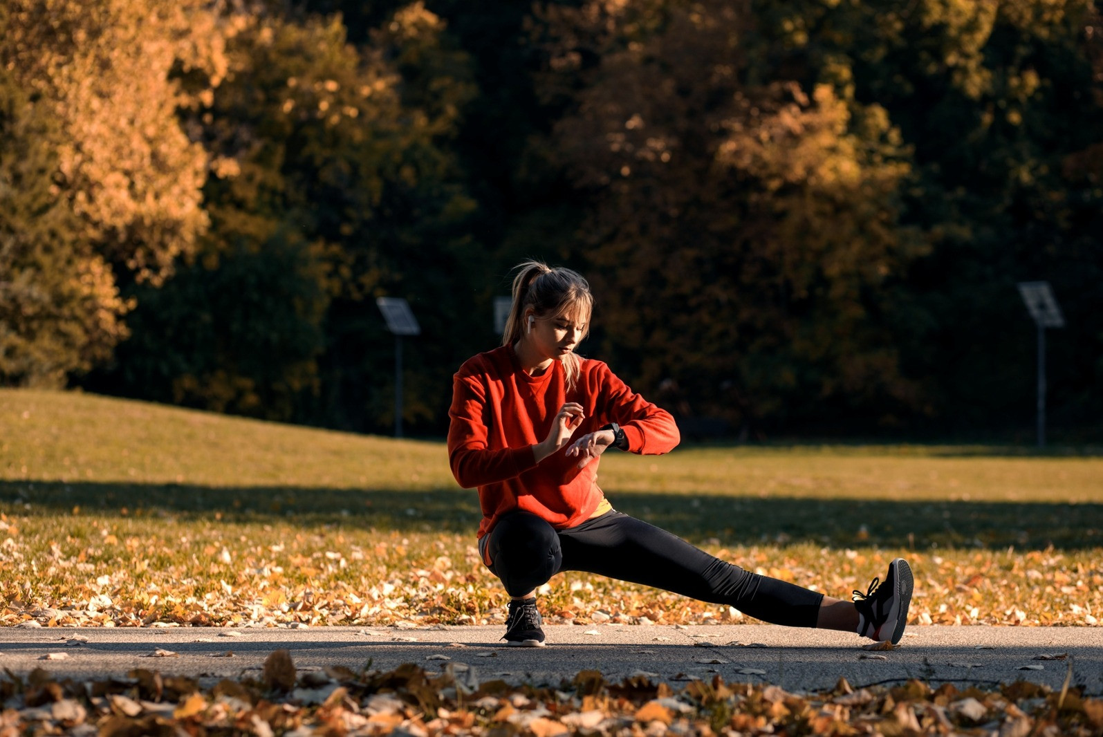 Woman pausing during an outdoor workout and checking her watch in a park.