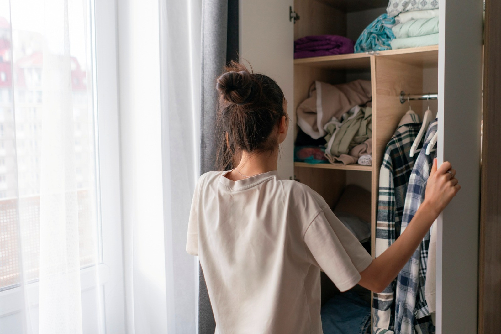 Woman choosing clothes from an open wardrobe in a bright bedroom