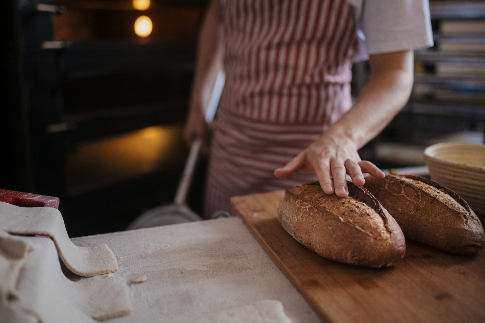 Baker placing a hand on freshly baked loaves of bread on a wooden board.