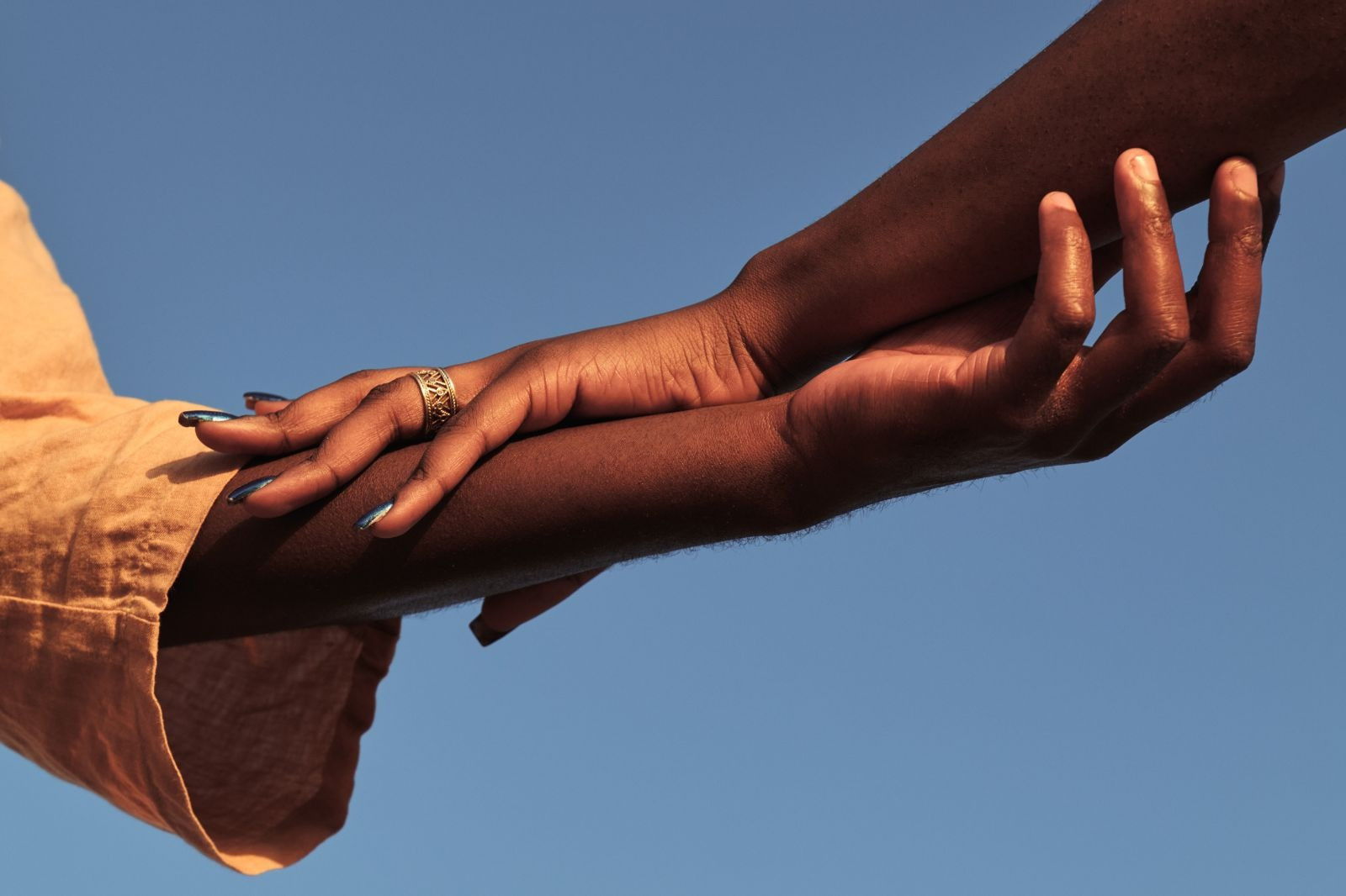 Close-up of two hands gently holding an arm against a clear blue sky, symbolizing comfort, support, and calm after EMDR therapy.