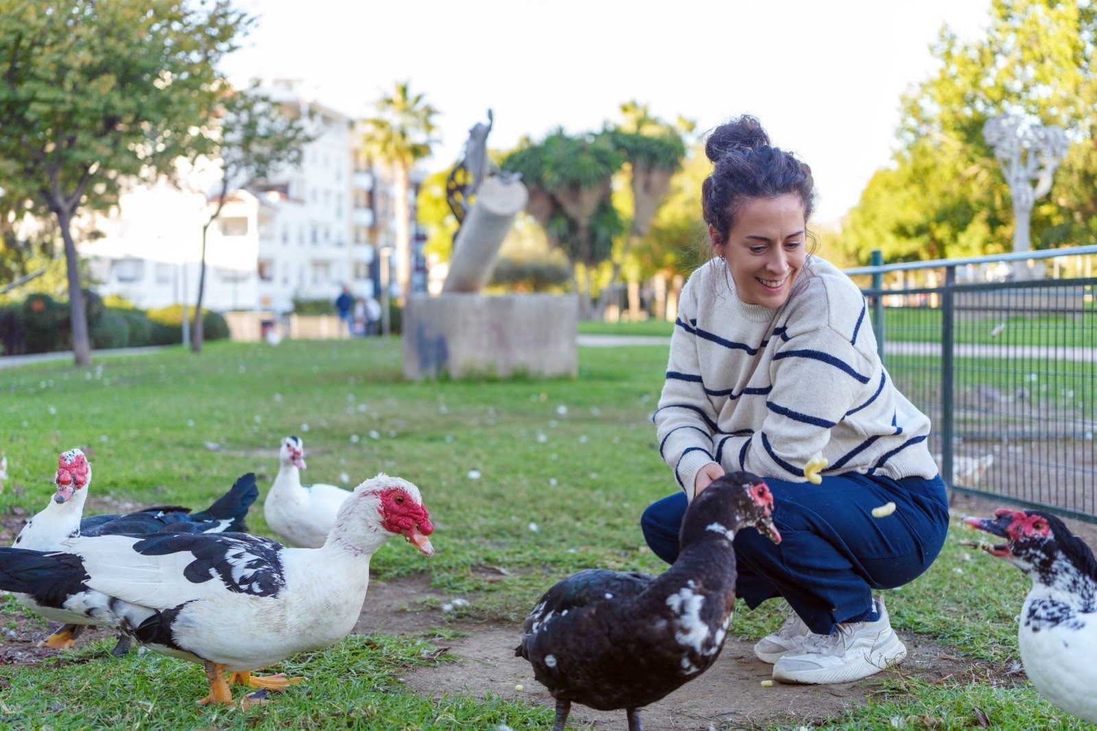 Woman crouching in a grassy park and smiling while feeding ducks.