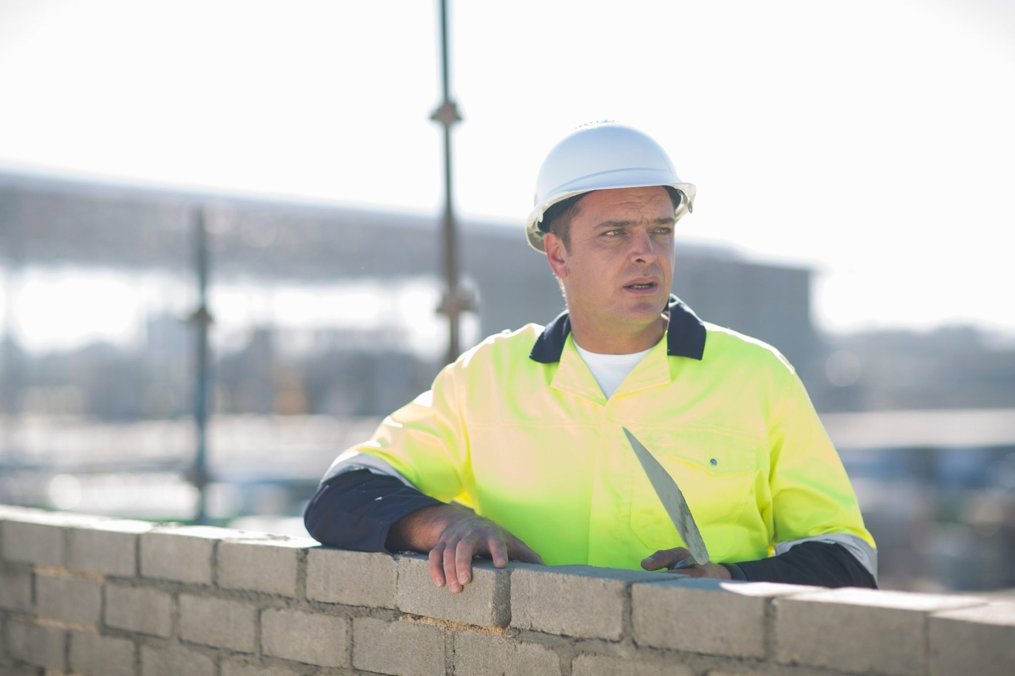 Construction worker in a hard hat and high-visibility shirt standing behind a brick wall