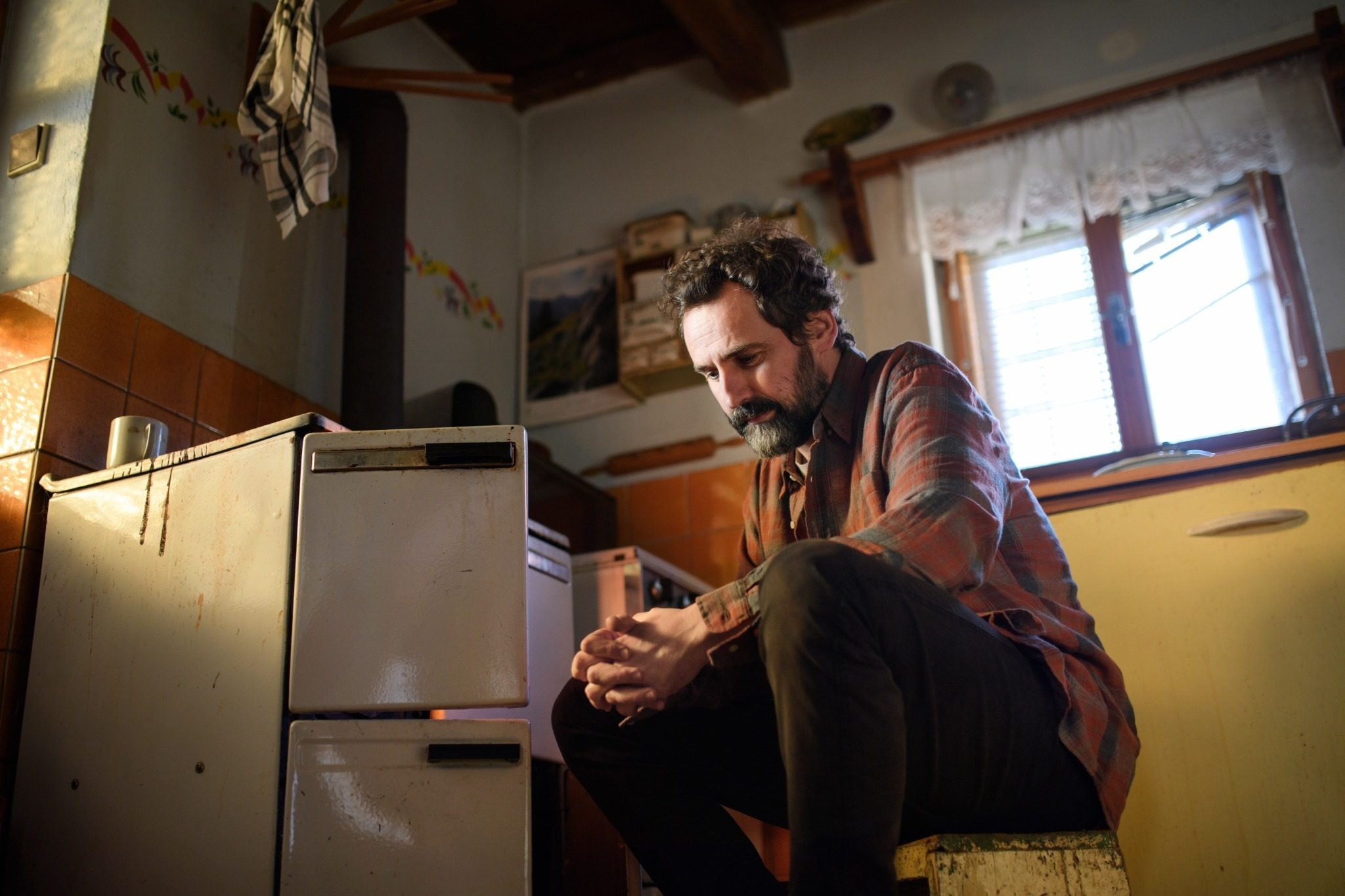 Man sitting indoors with his hands clasped and looking down thoughtfully