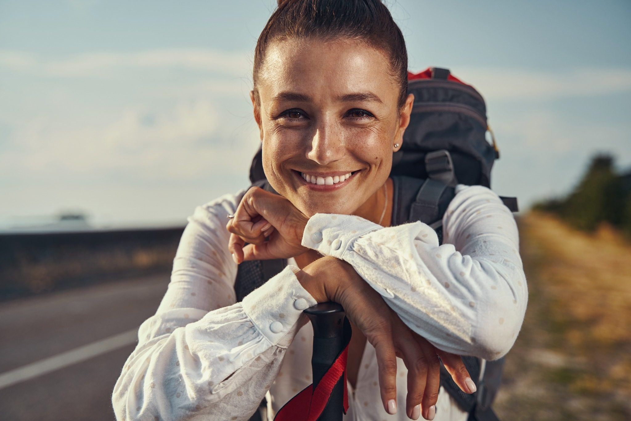 Smiling woman with a backpack resting beside a road