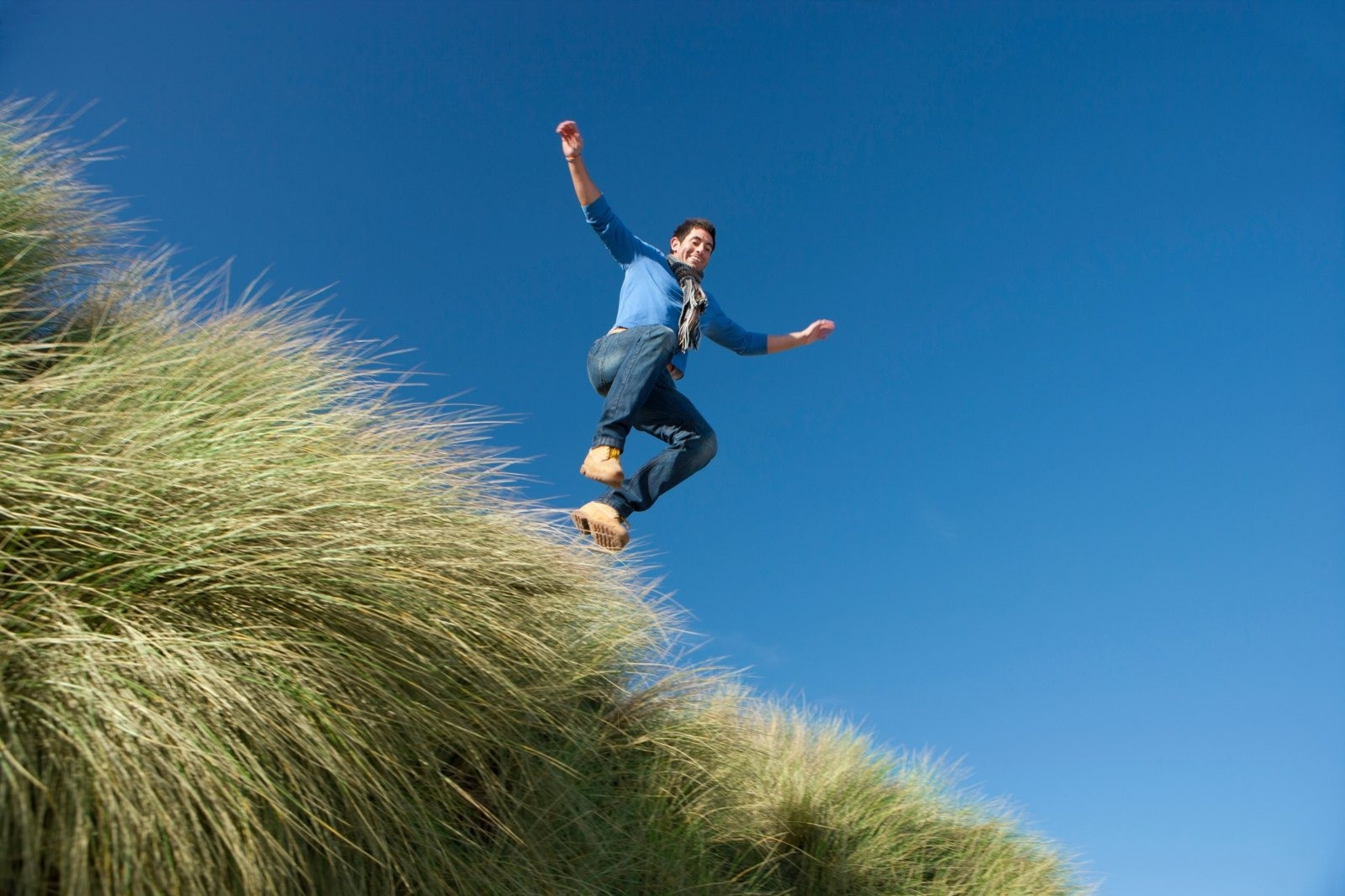 Man jumping above a grassy hillside beneath a clear blue sky.