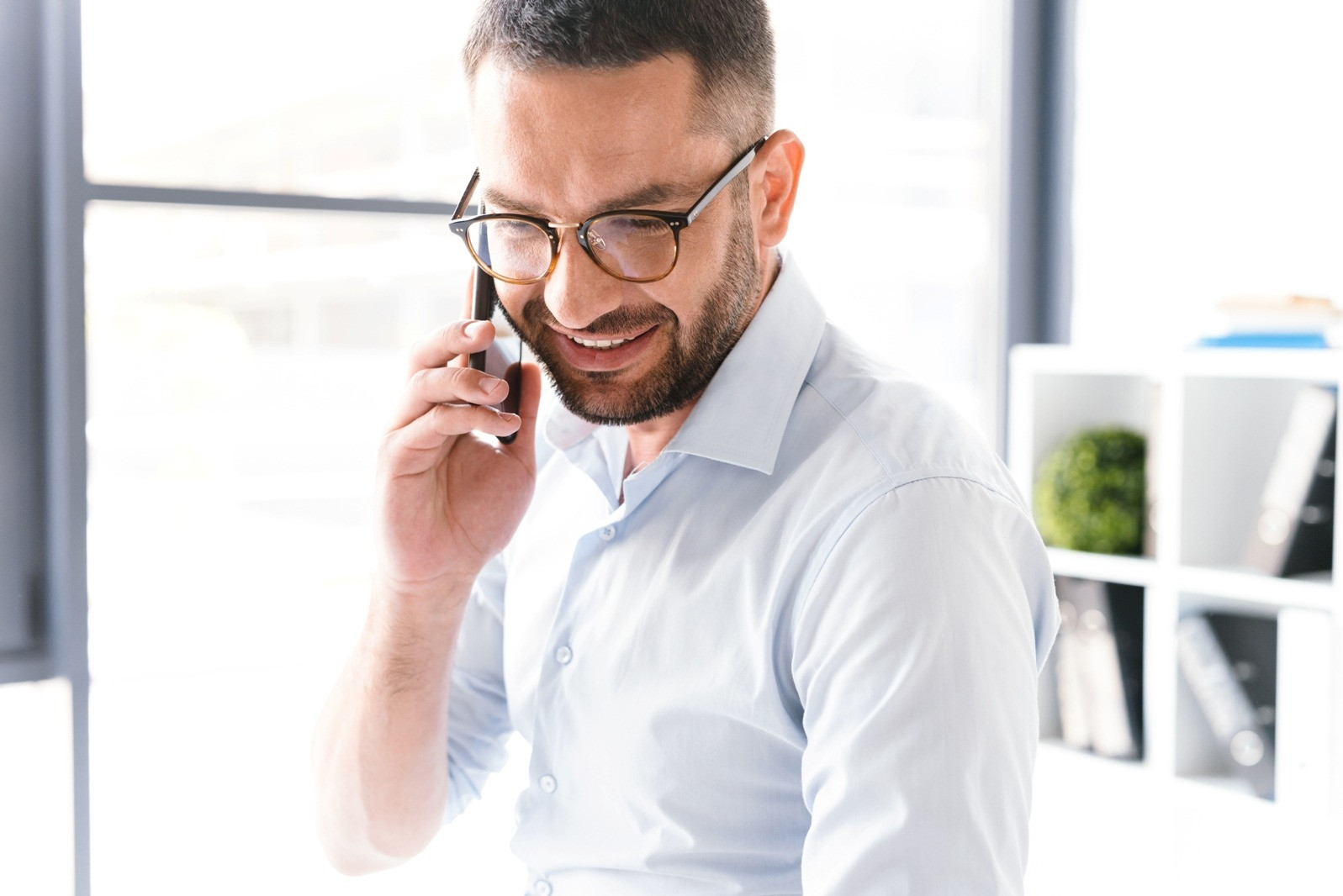 Smiling man wearing glasses talking on the phone in a bright office, illustrating a positive change in mood.