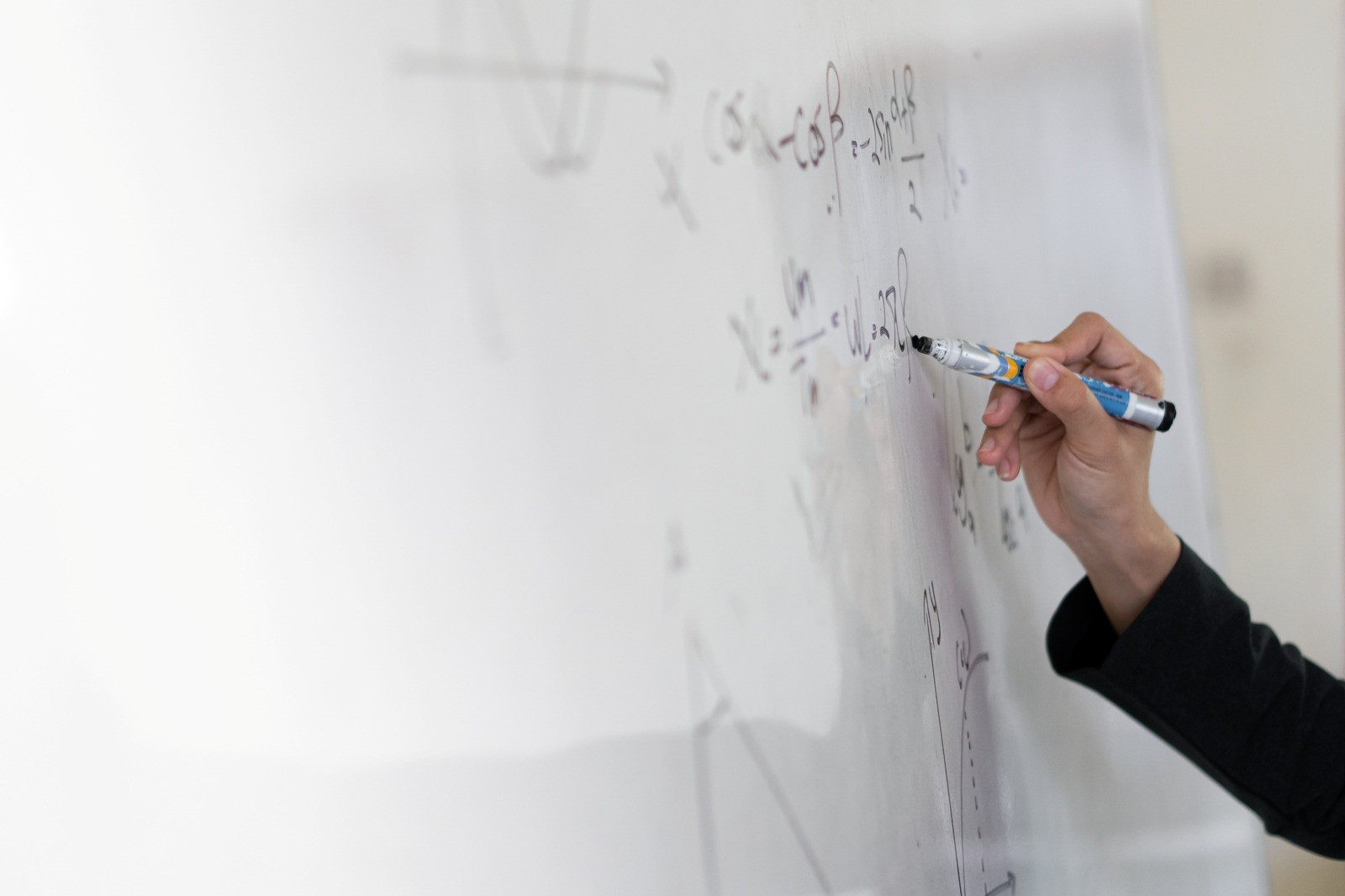 Close-up of a person writing mathematical equations on a whiteboard with a marker.