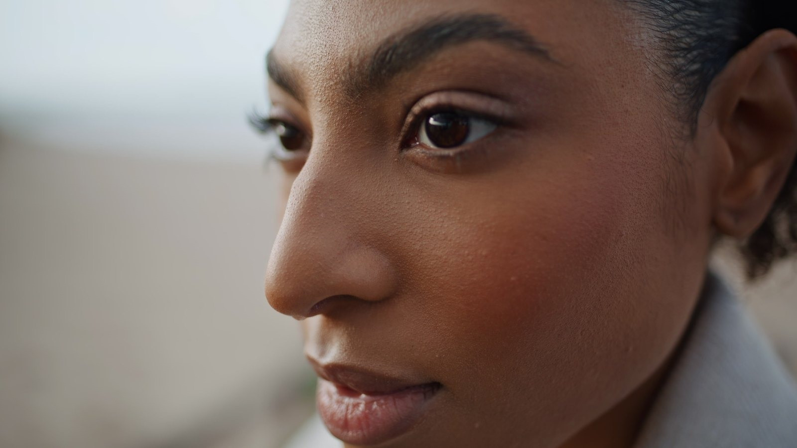 Close-up portrait of a woman with dark hair looking thoughtfully to the side against a softly blurred background.