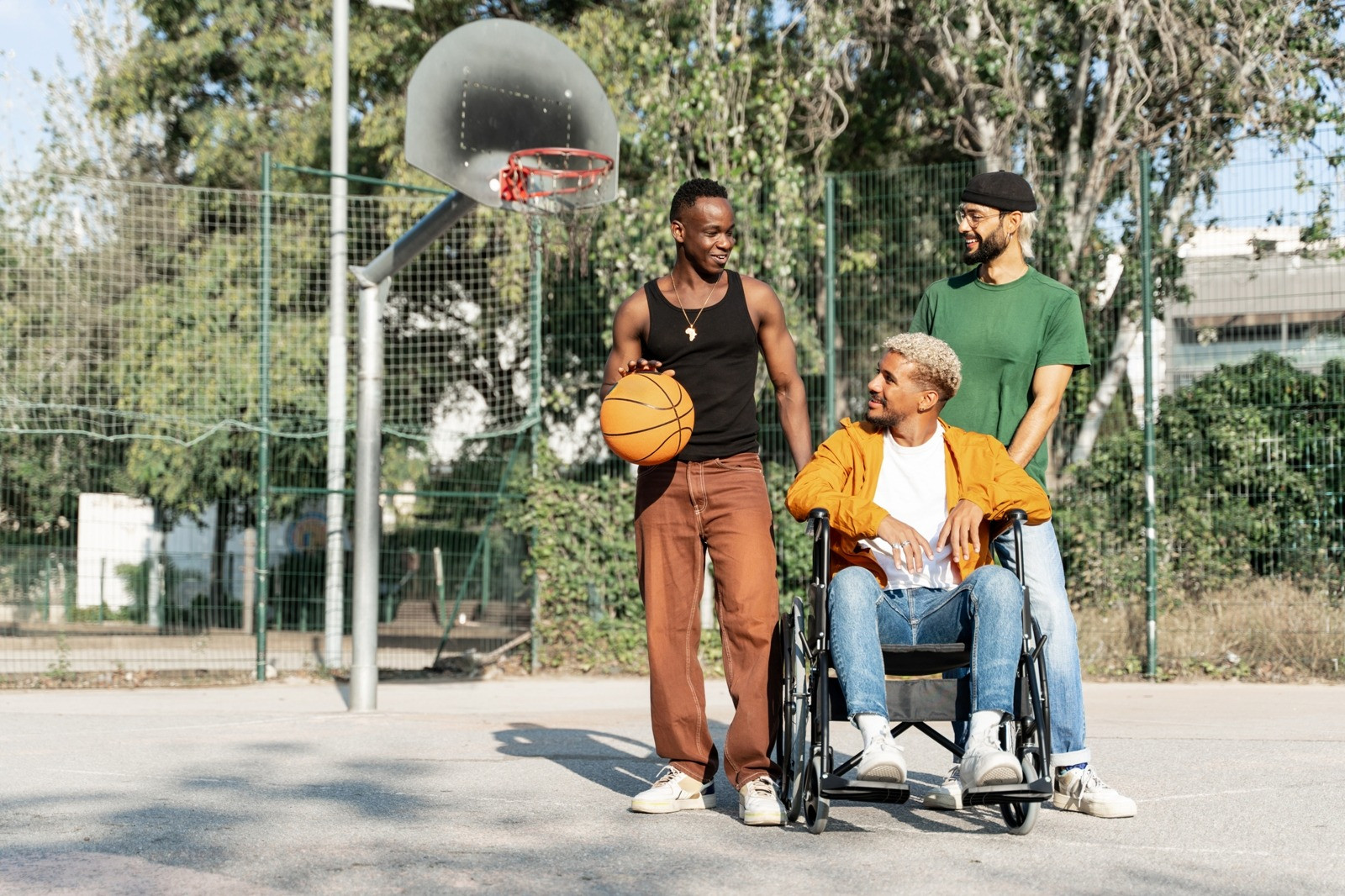 Three men spending time together on an outdoor basketball court, including one man using a wheelchair.