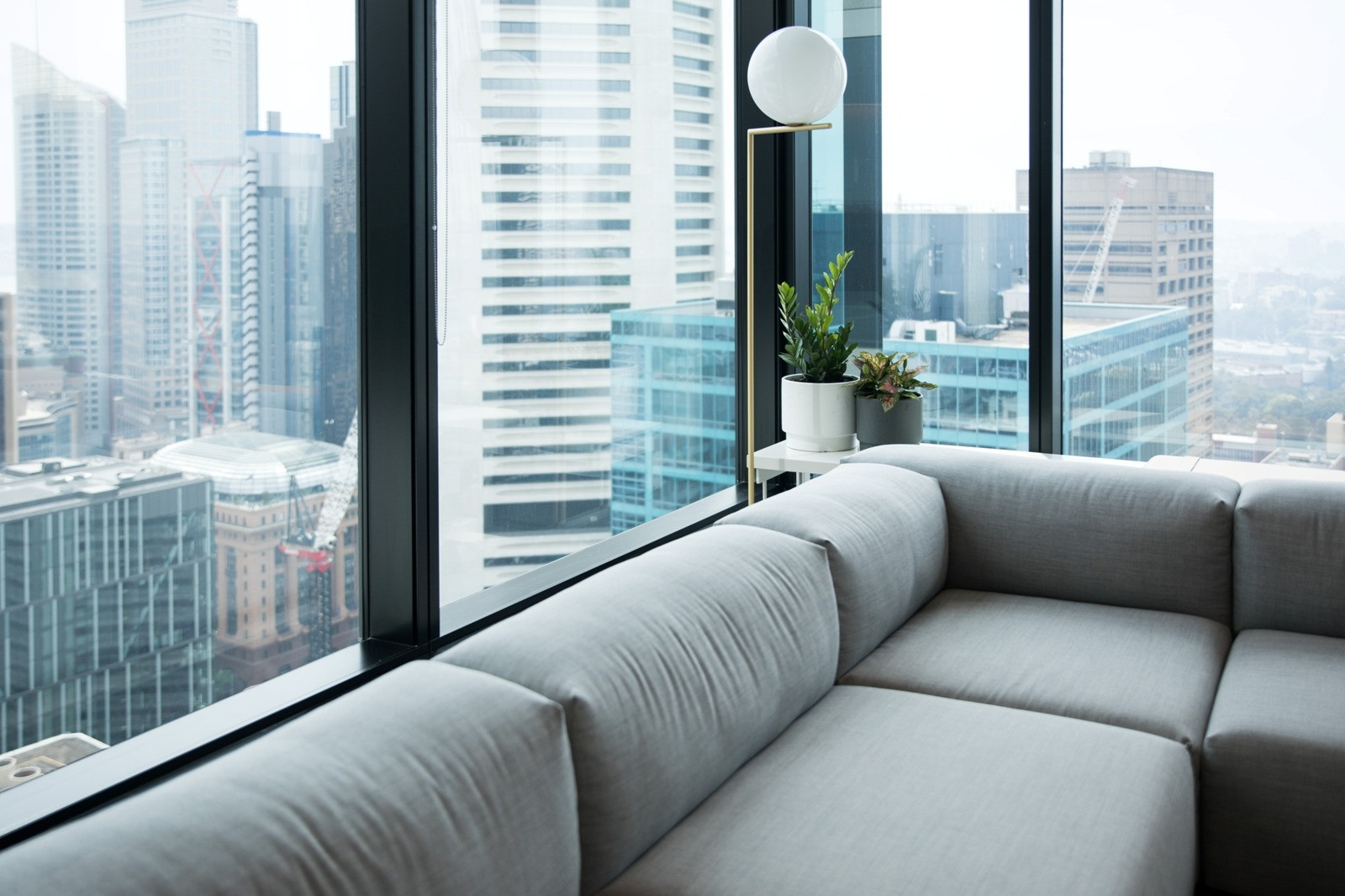 Modern seating area with a gray sofa beside large windows overlooking a city skyline