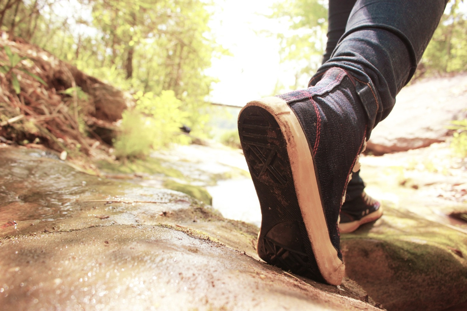 Close-up of a person walking across a rocky outdoor path in casual shoes.