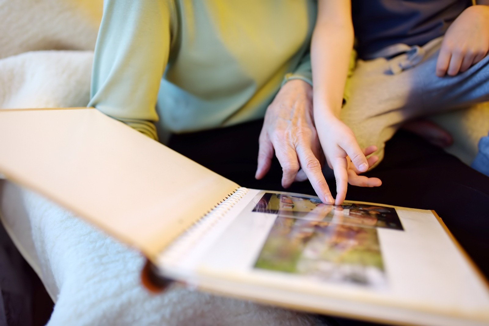 Adult and child looking through a photo album together while seated on a sofa.