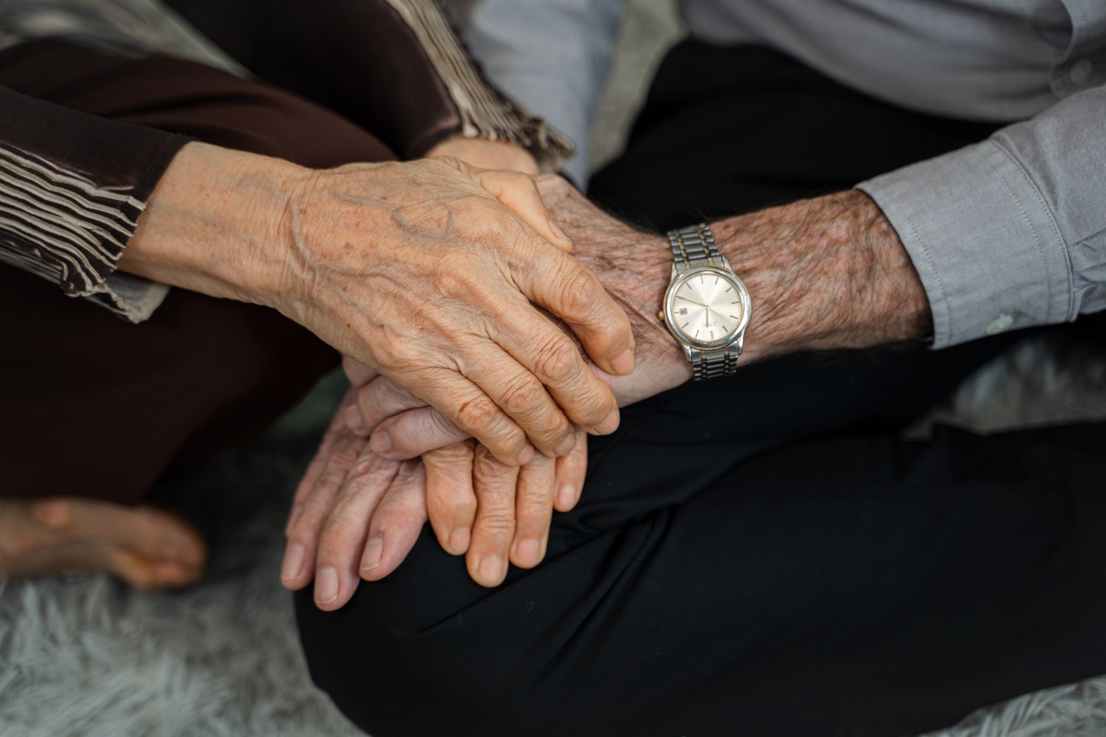 Close-up of two older adults holding hands, with a wristwatch visible on one person's wrist.