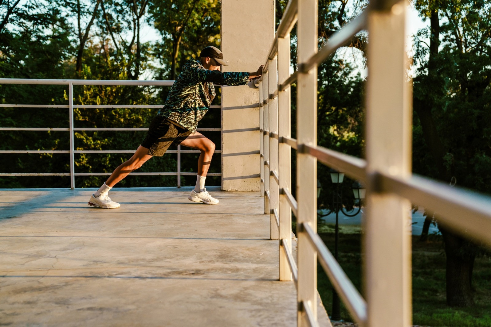 Man stretching outdoors with both hands against a wall on a sunlit terrace.