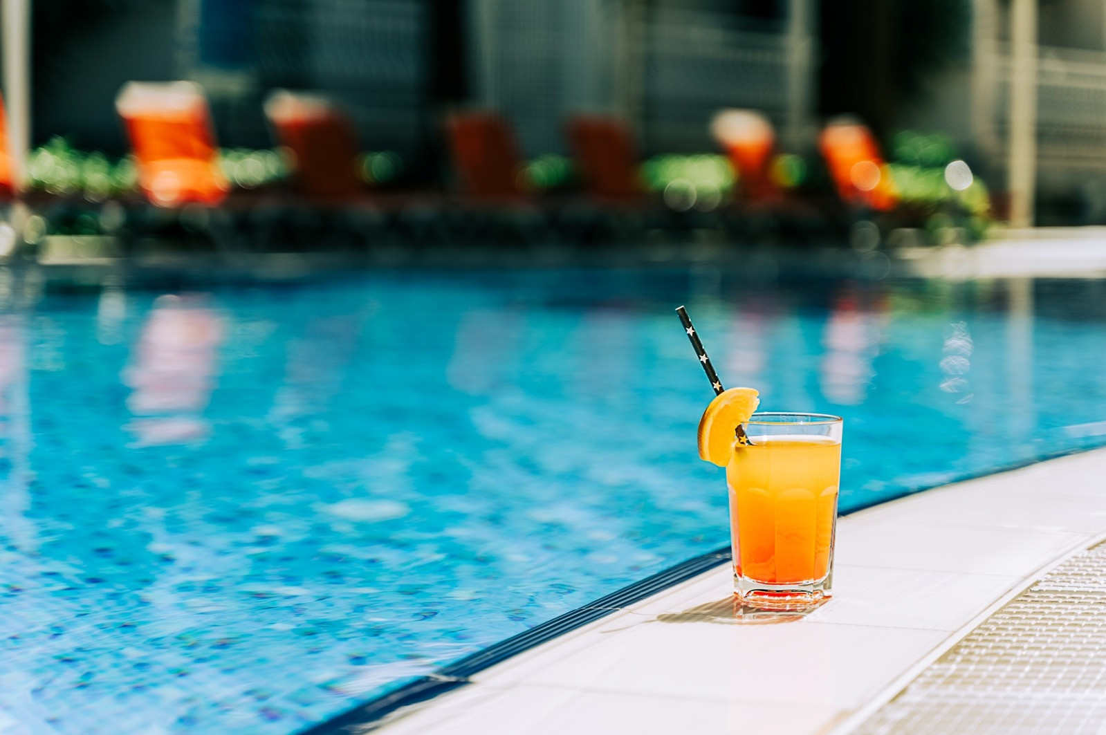 Orange drink beside a swimming pool with blurred lounge chairs in the background.