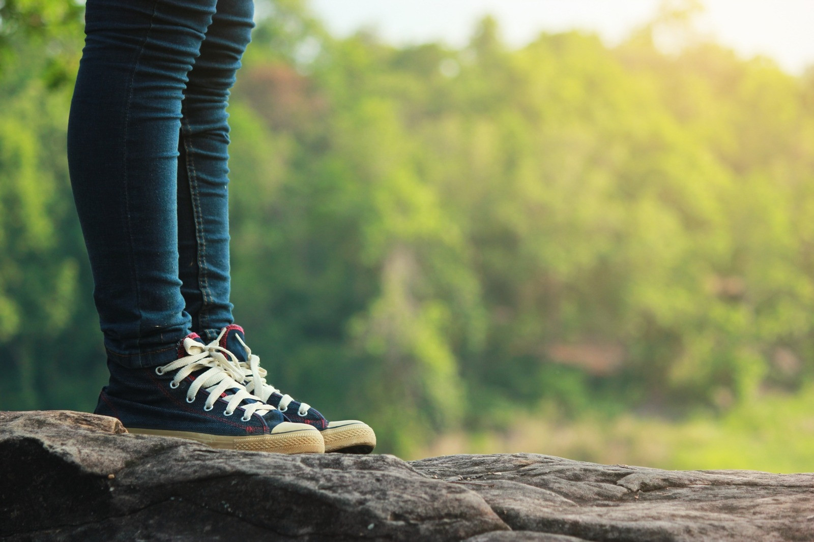 Person standing on a rock outdoors in sneakers, with a softly blurred green landscape in the background.