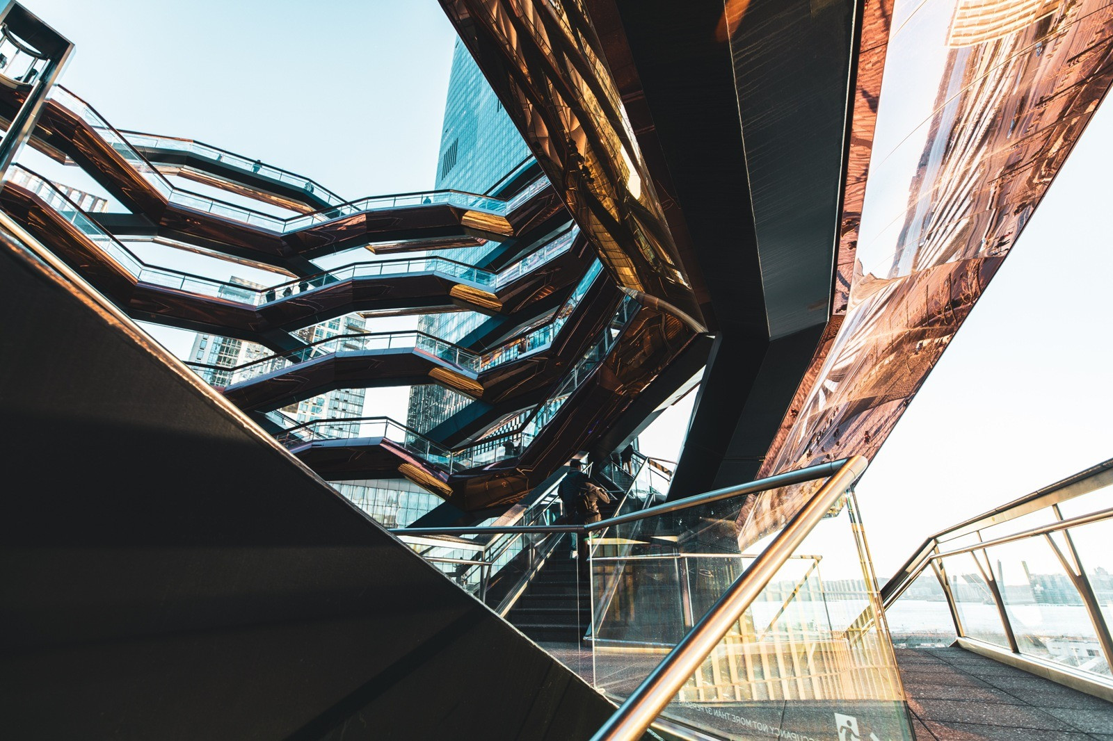 Looking upward through interconnected staircases with copper-colored surfaces and glass railings.