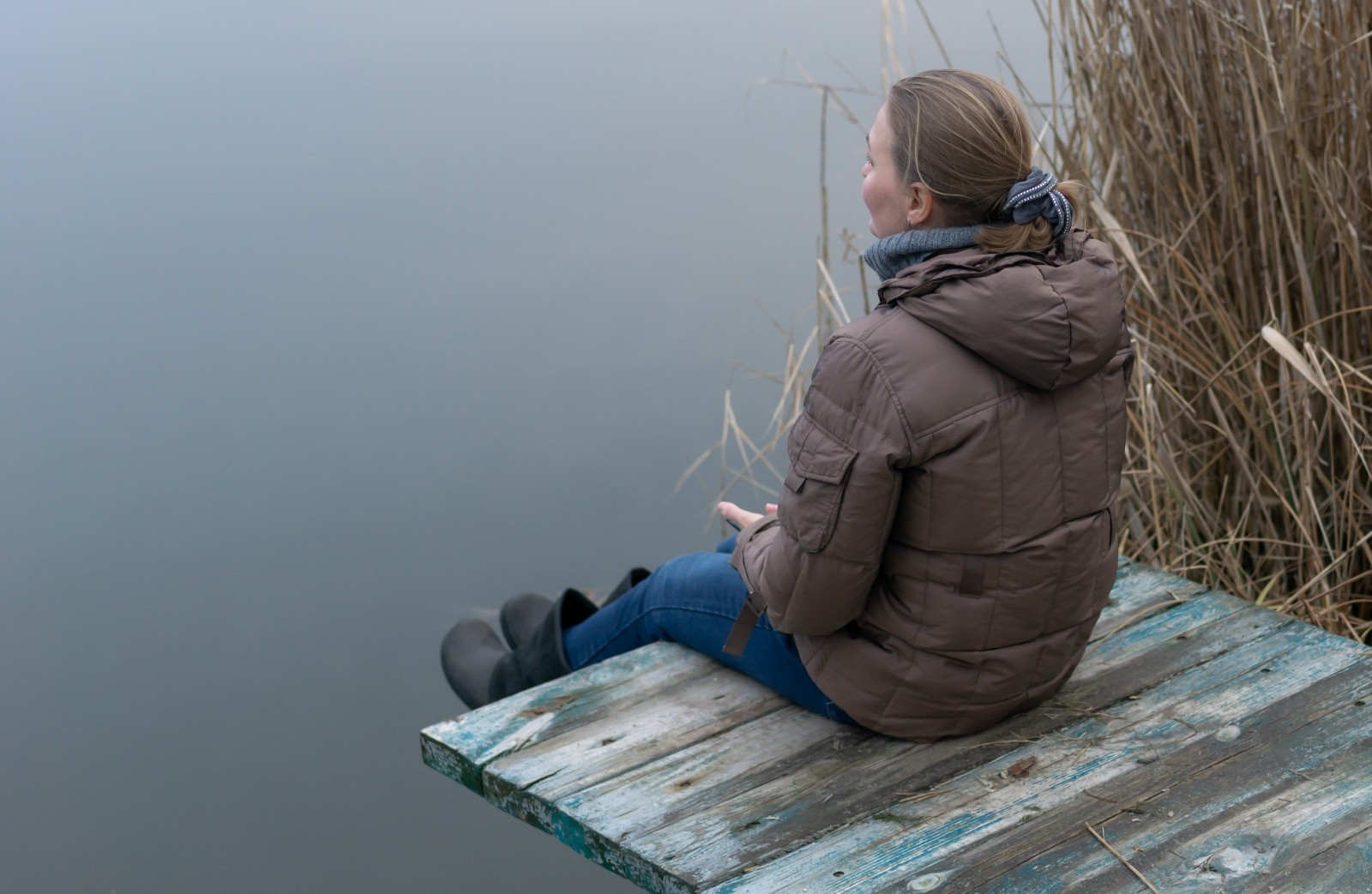 Woman sitting quietly by a lake, taking a reflective break in a calm outdoor setting.