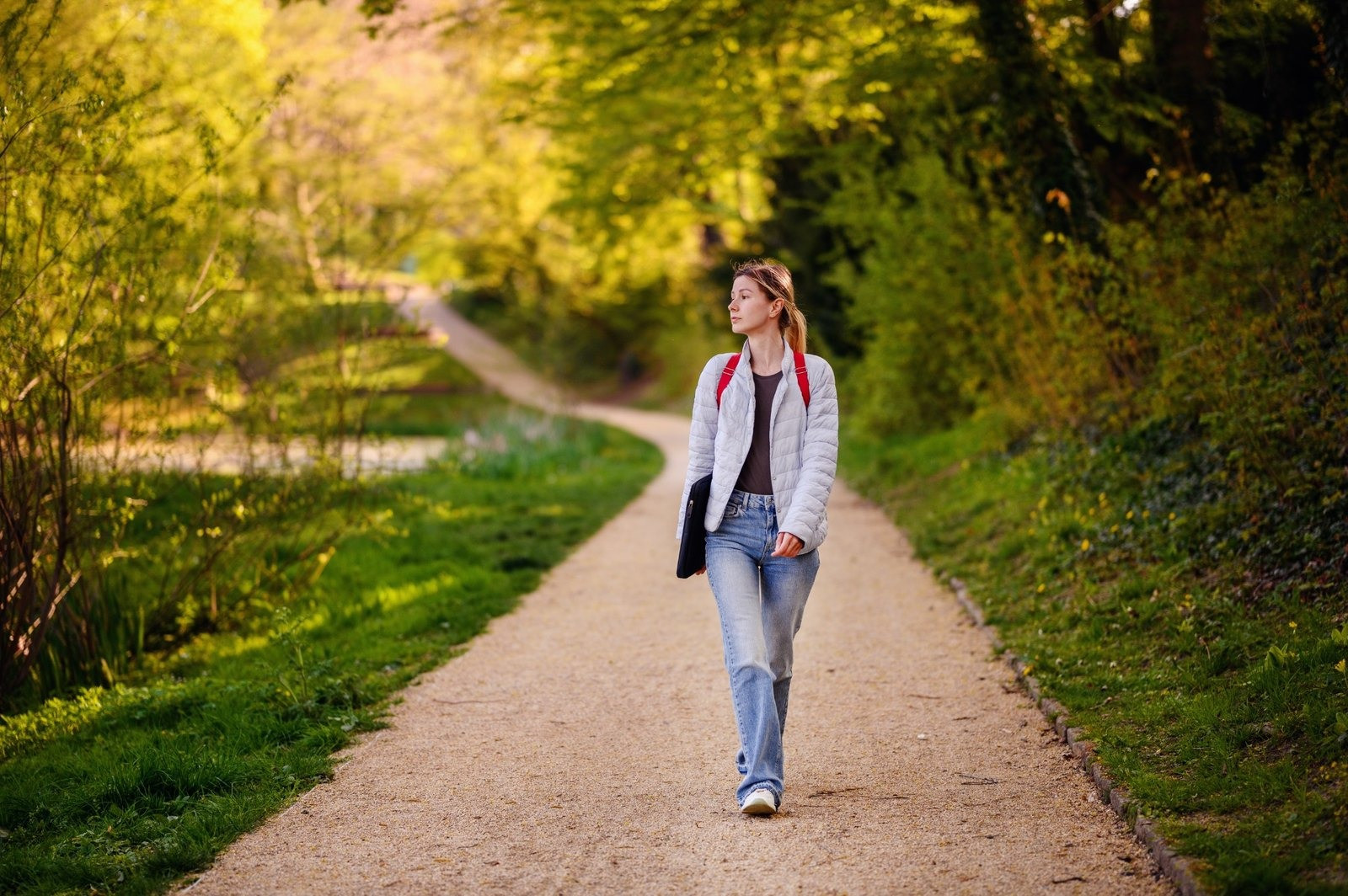 Woman with a backpack walking along a path through a green wooded park