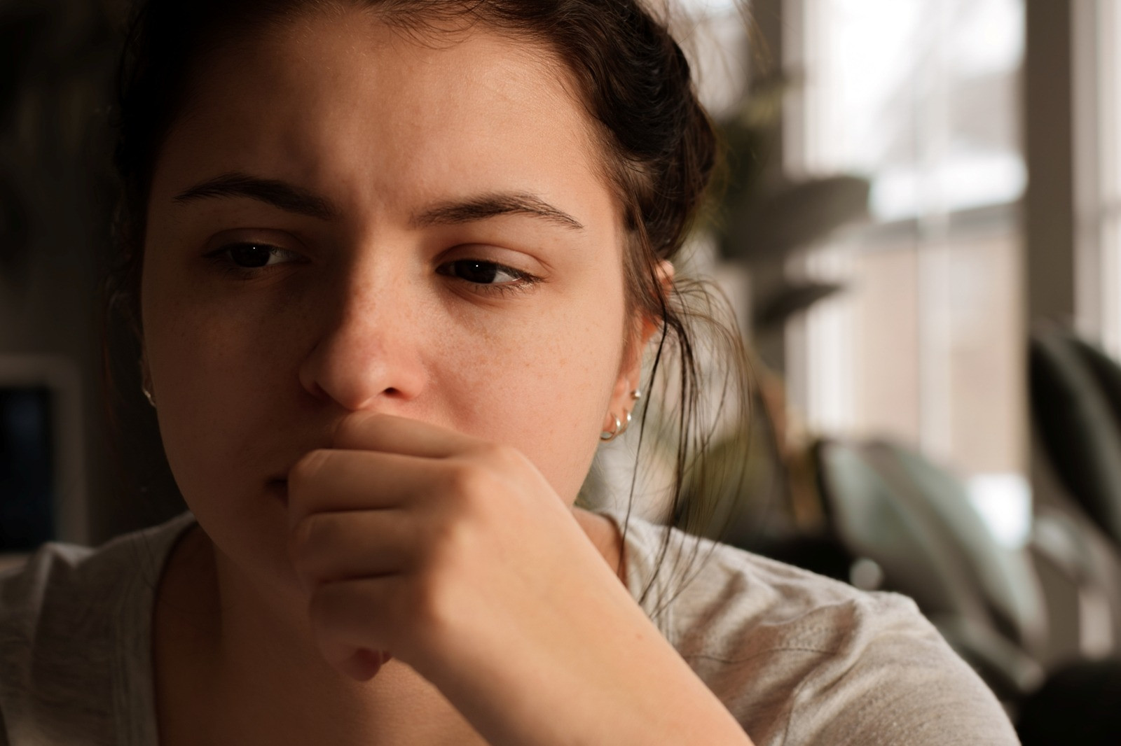 Thoughtful woman sitting indoors in a quiet setting, representing focus and privacy for a self-guided EMDR session.