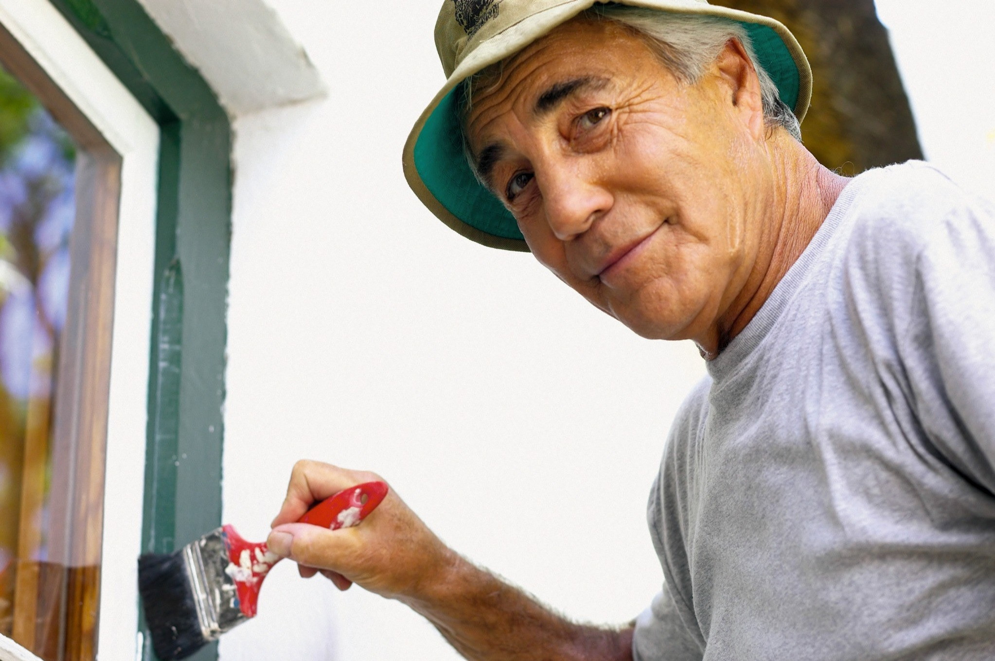 Older man painting around a window with a paintbrush
