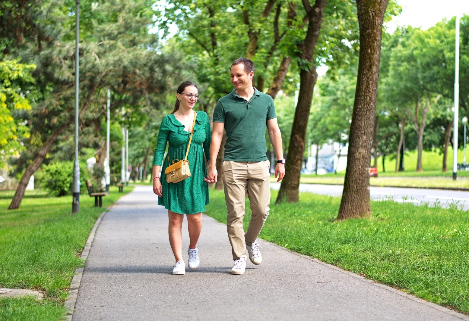 Man and woman walking together along a tree-lined park path.