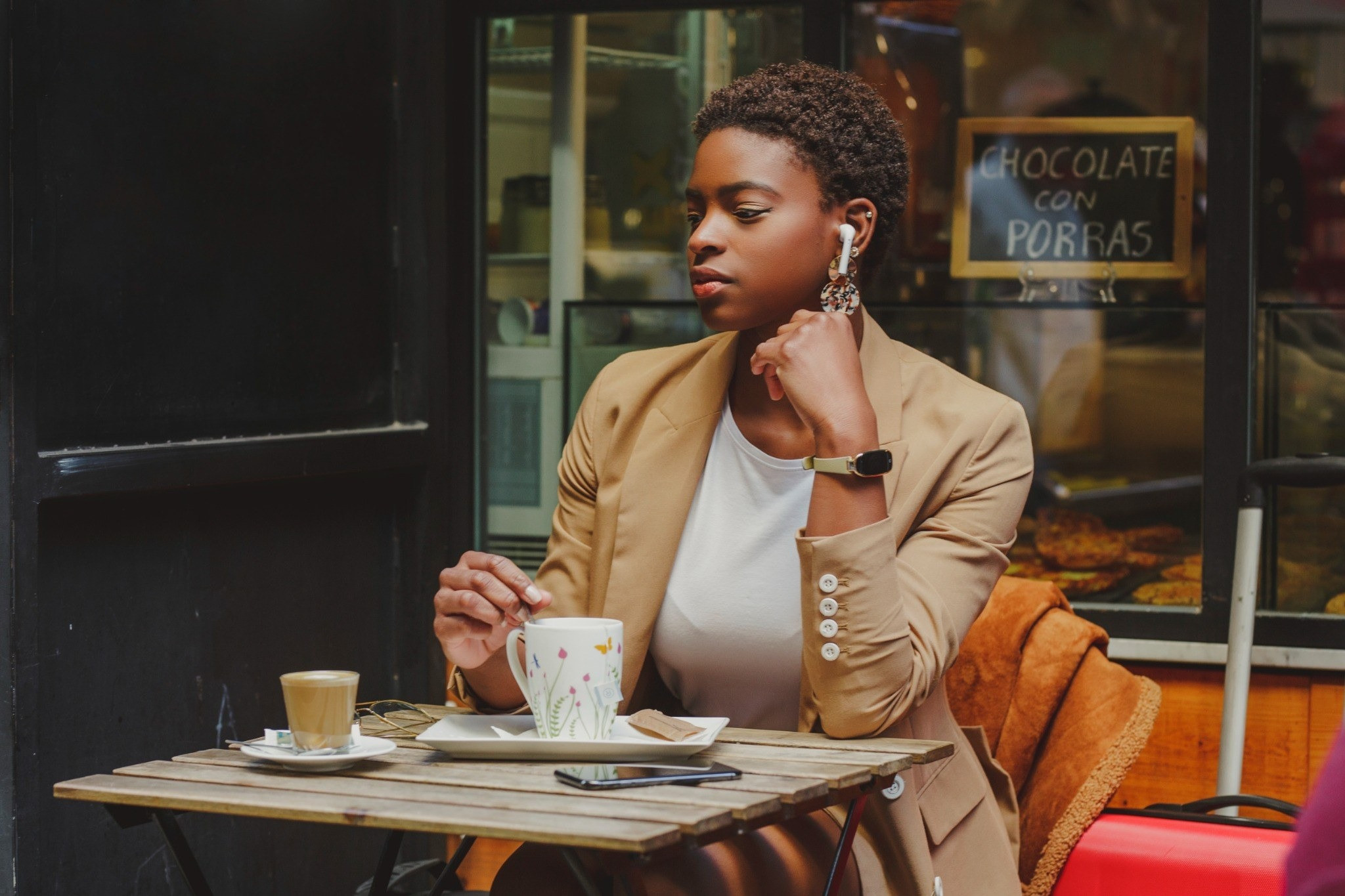Woman wearing earbuds sitting at an outdoor café with a cup of tea