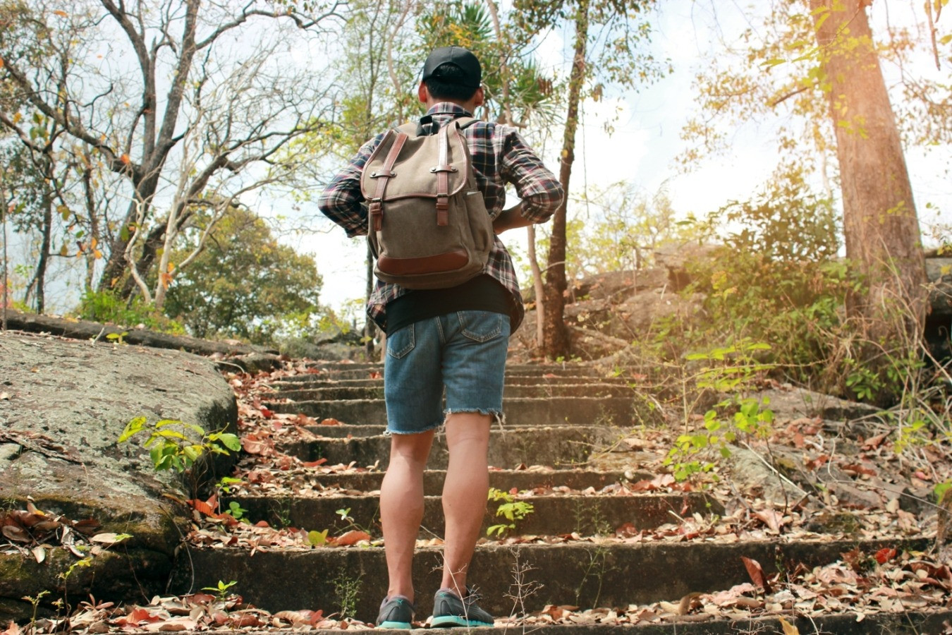 Person with a backpack climbing outdoor steps through a wooded area, representing the ongoing effort of living with chronic pain.