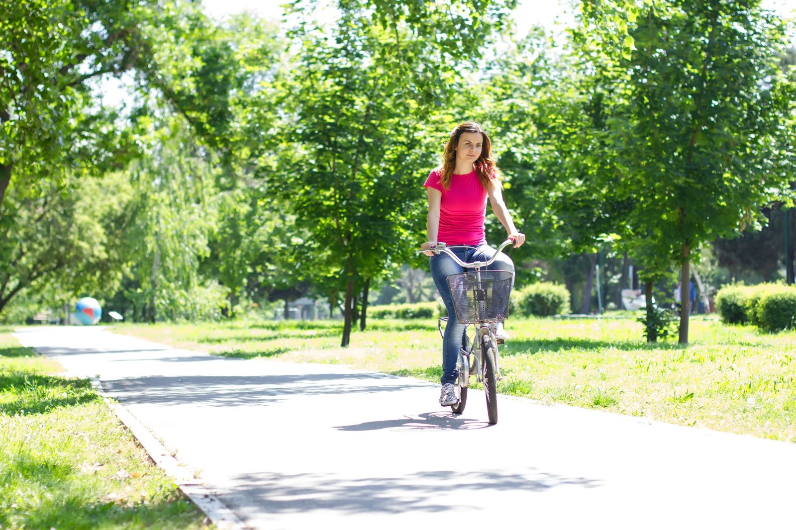 Woman riding a bicycle along a sunlit path through a green park.