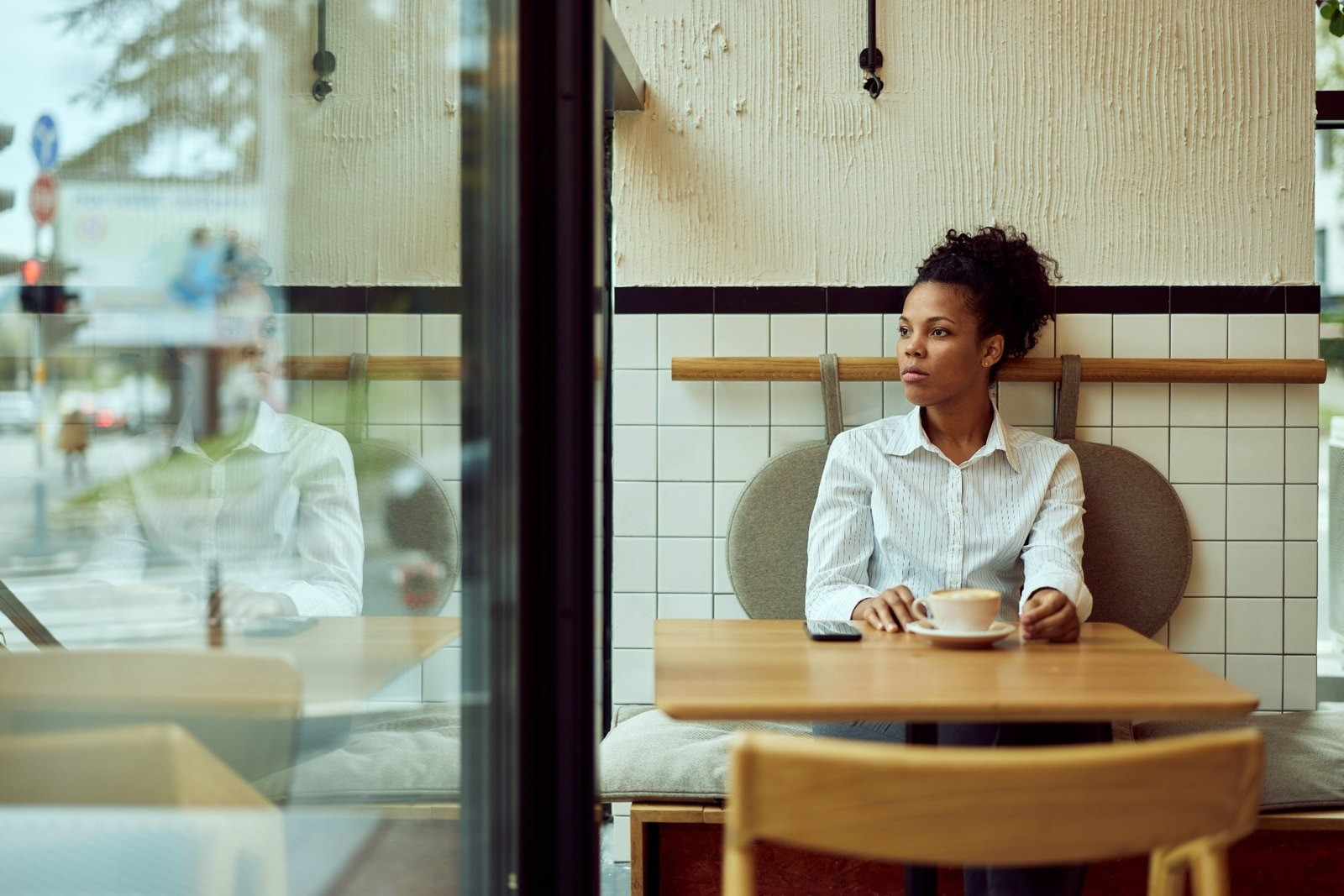 Woman sitting at a café table with a cup while wearing comfortable everyday clothing
