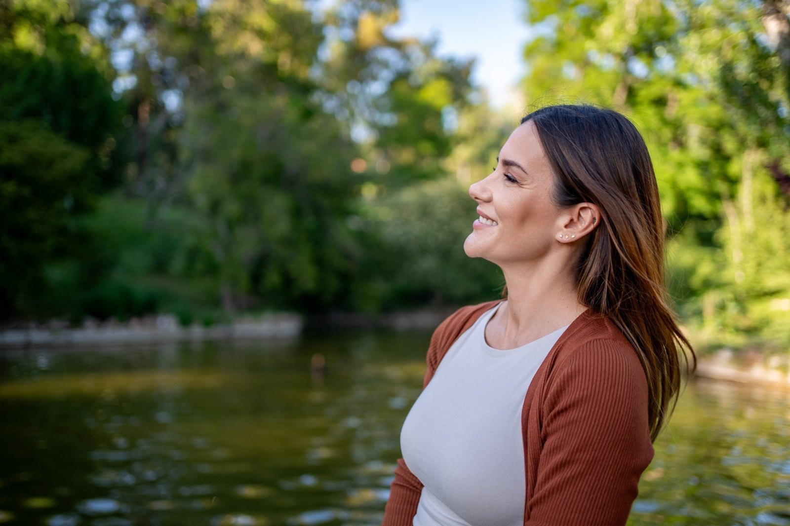 Woman smiling outdoors beside a lake surrounded by trees
