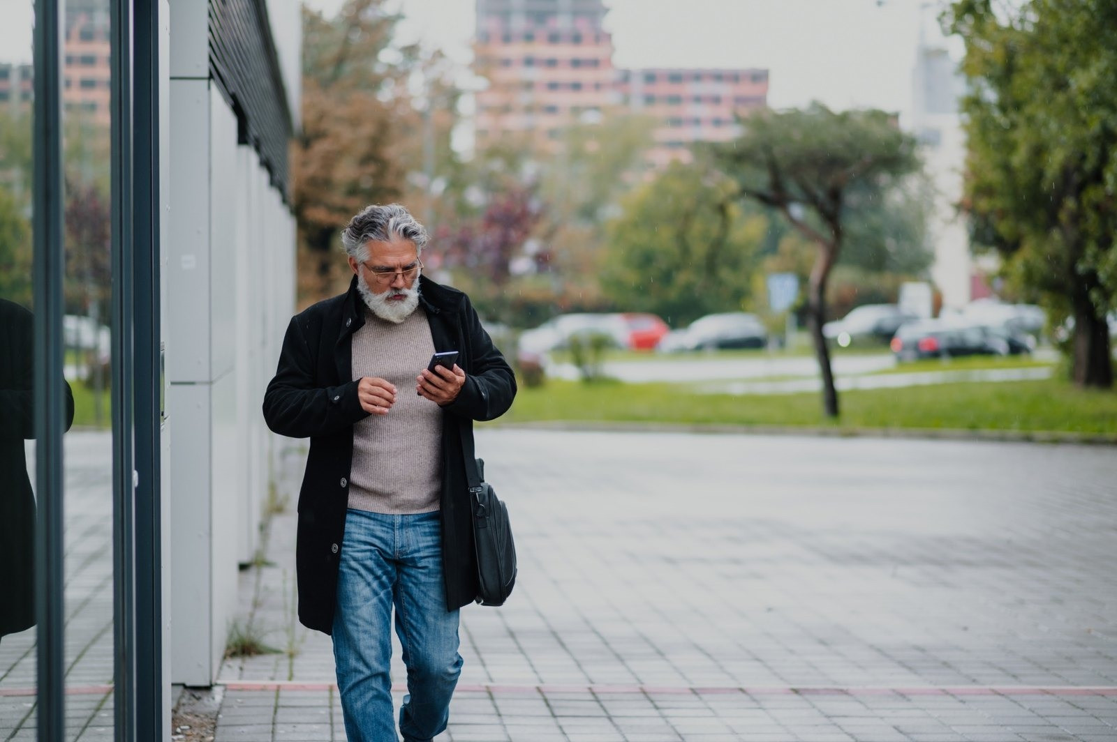 Older man looking at his smartphone while walking outdoors on a city sidewalk