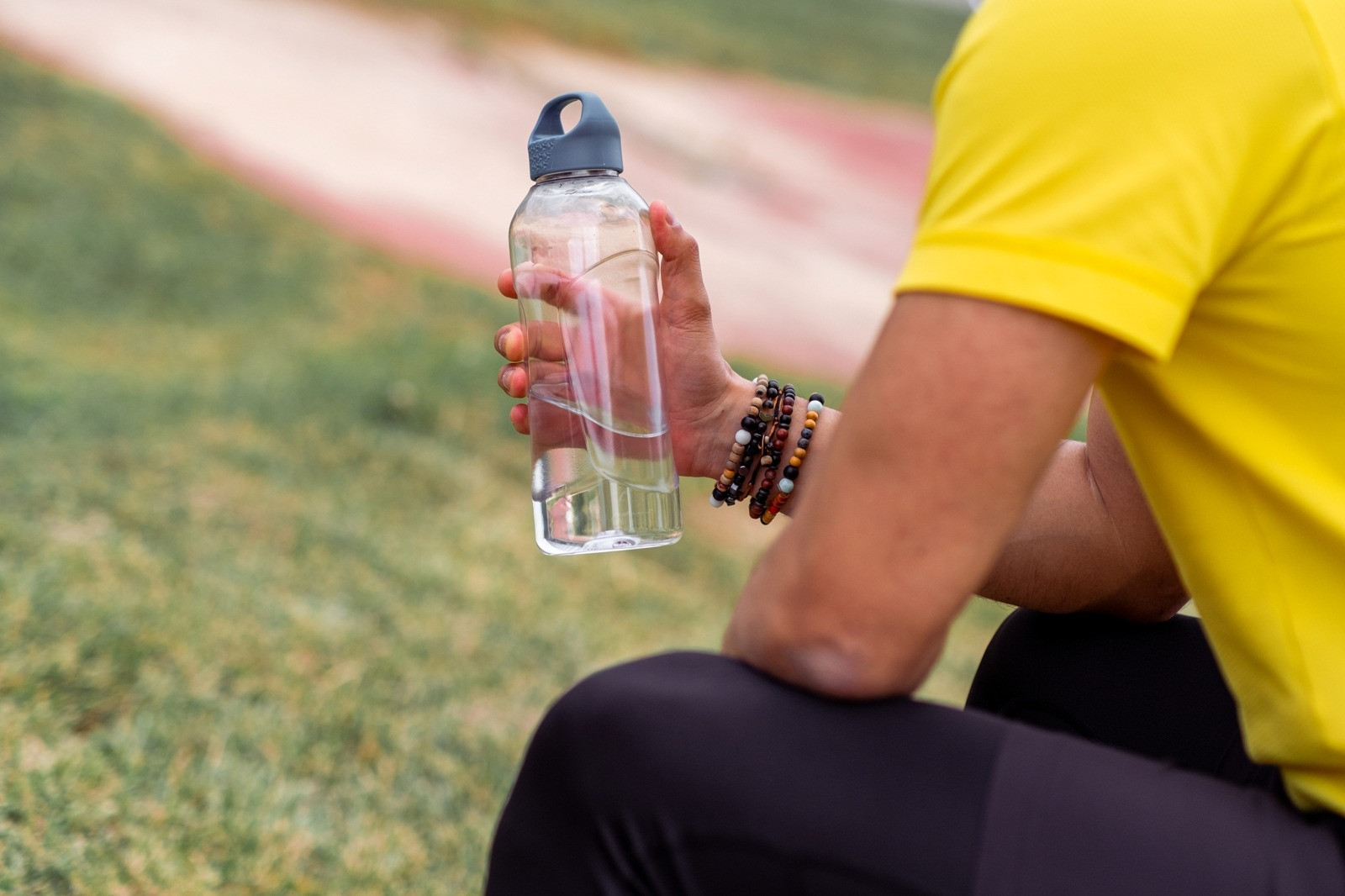 A person in a yellow shirt sitting outdoors and holding a clear water bottle.