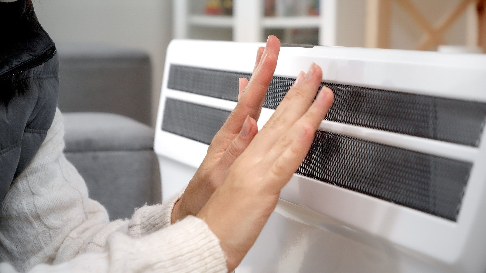 Person warming their hands in front of a portable electric heater indoors