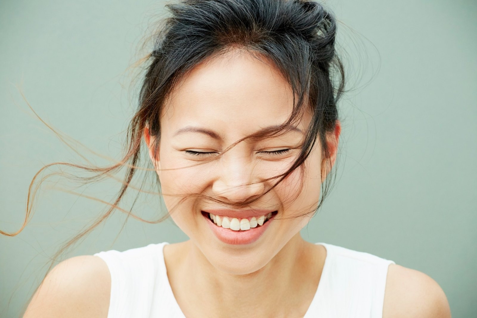Close-up portrait of a smiling woman with her eyes closed and strands of hair blowing across her face.