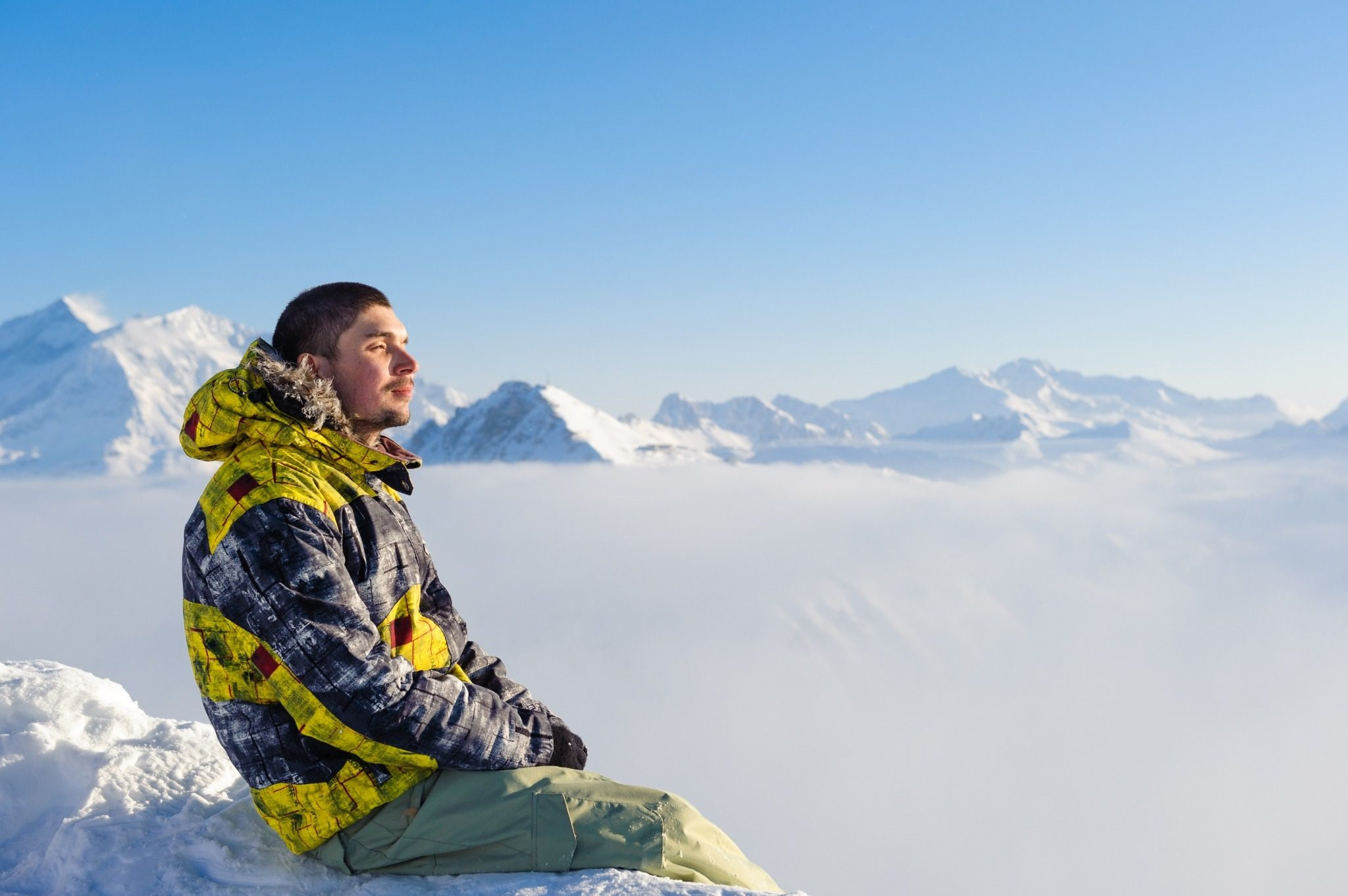Man sitting in the snow overlooking a mountain landscape