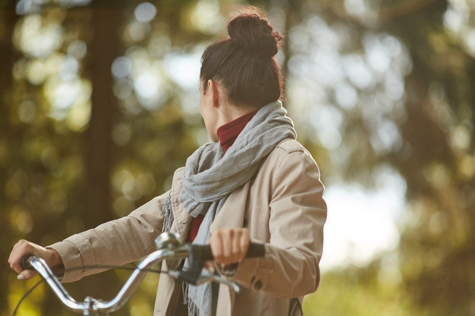 Woman holding a bicycle outdoors in a wooded area, pausing and looking back in warm natural light.