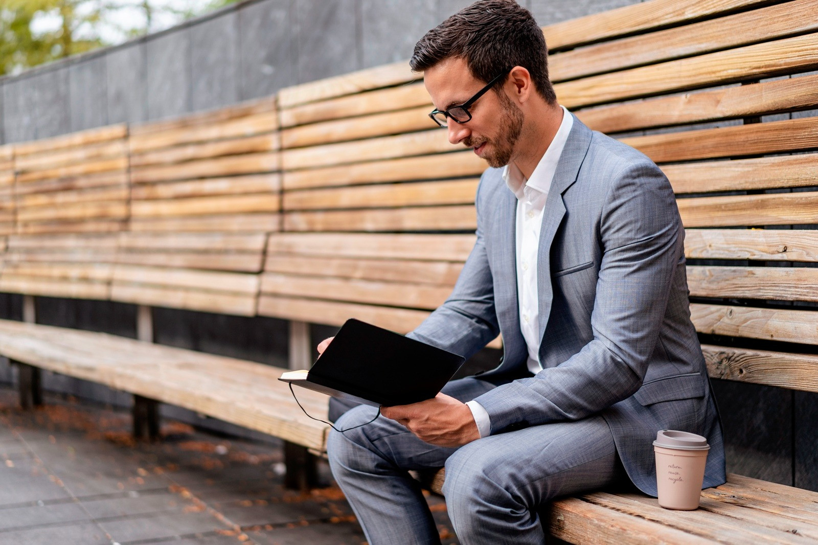 Man sitting on a bench with a notebook and coffee, taking a quiet moment after feeling overwhelmed.