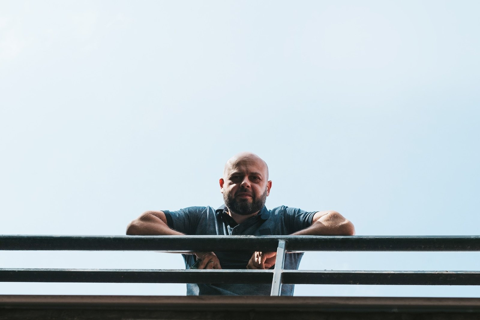 Man leaning on an outdoor railing against a clear blue sky