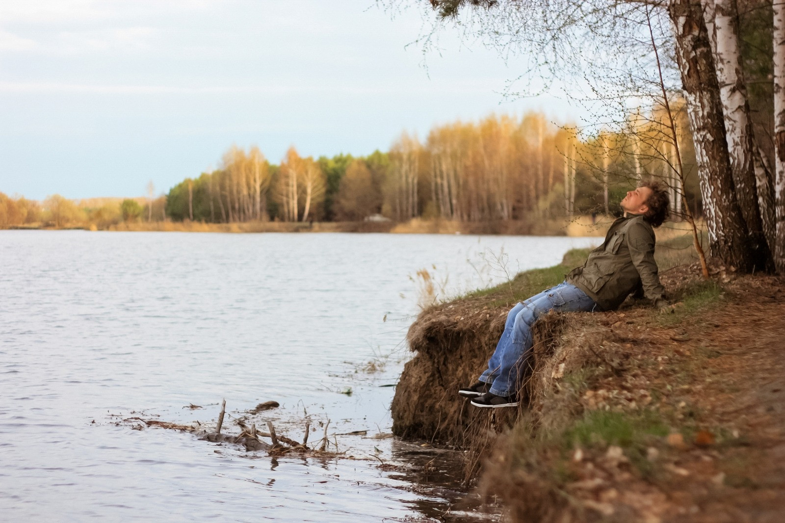 Man sitting quietly beside a lake and taking a reflective break in a peaceful outdoor setting.