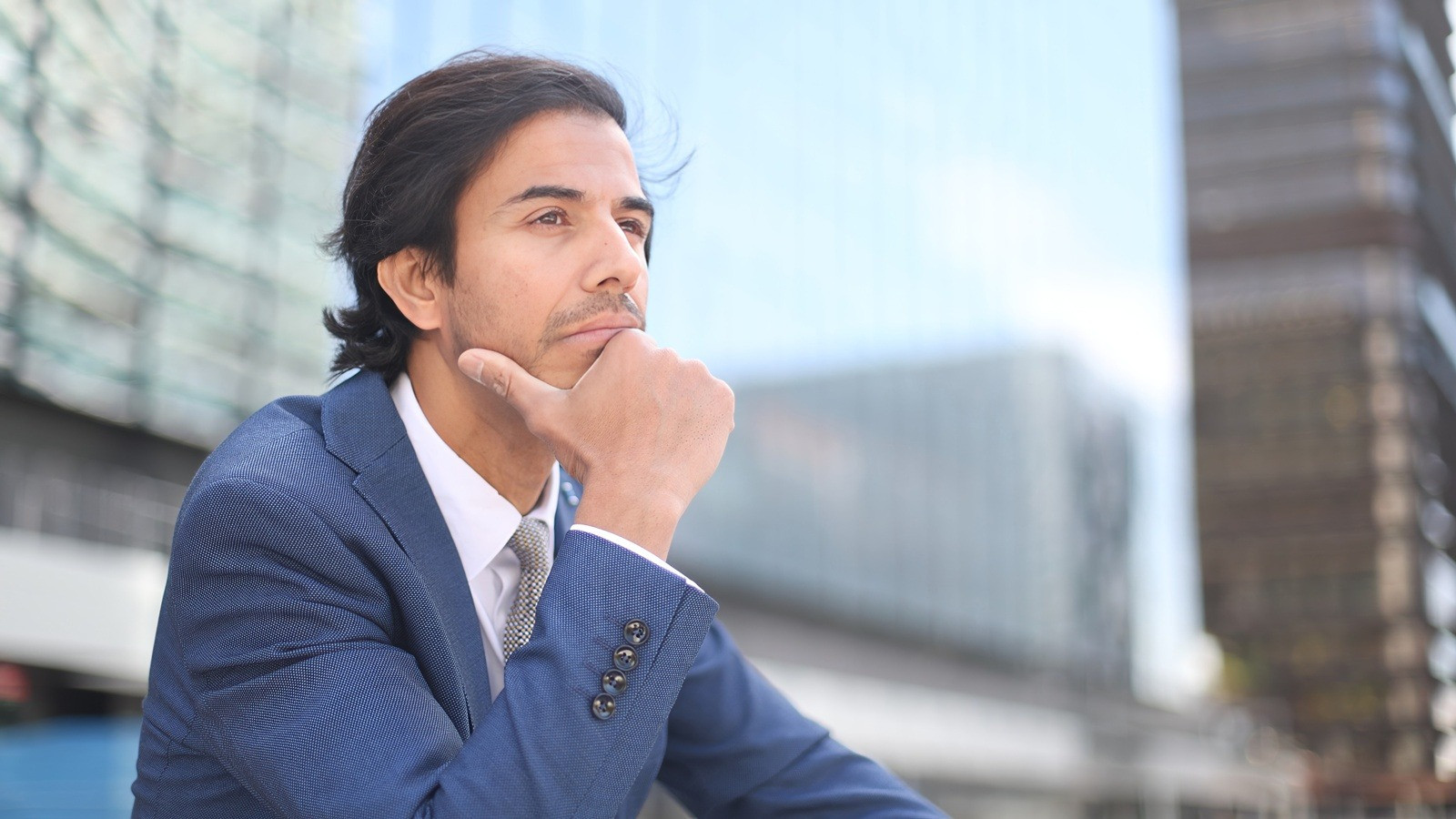 Thoughtful man in a suit sitting outdoors and looking ahead, illustrating a reflective or restless state.