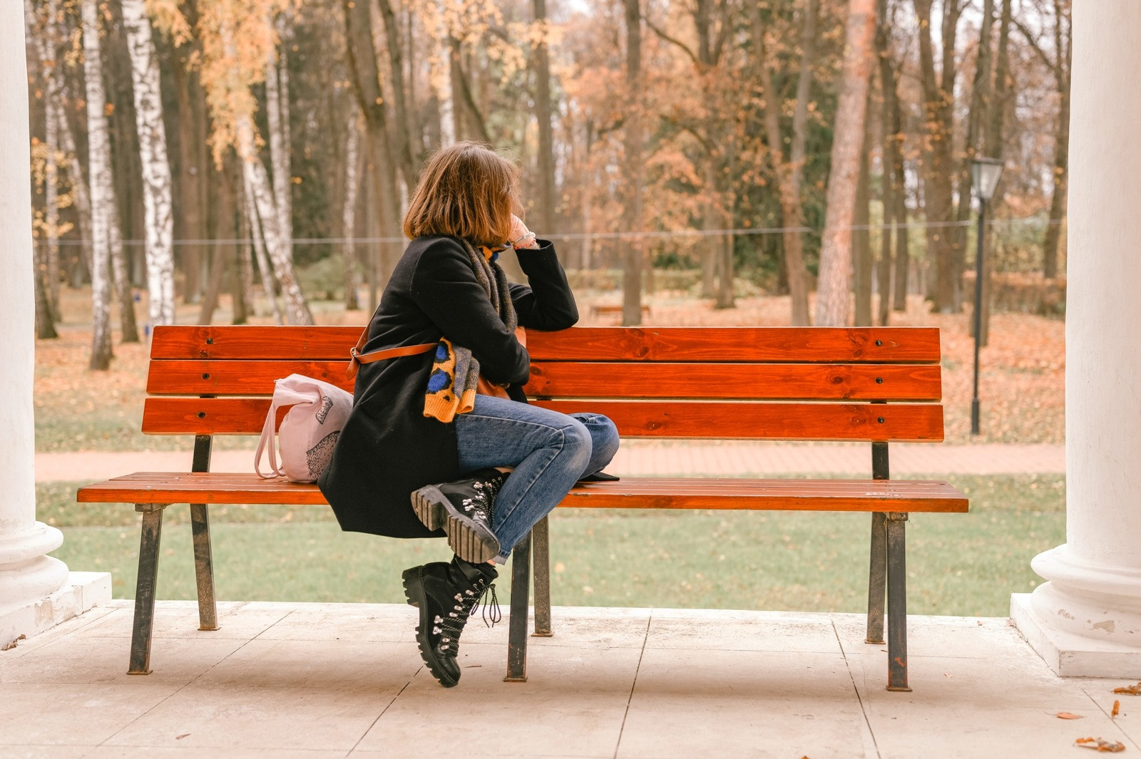 Woman sitting alone on a park bench in an autumn setting, looking away thoughtfully.