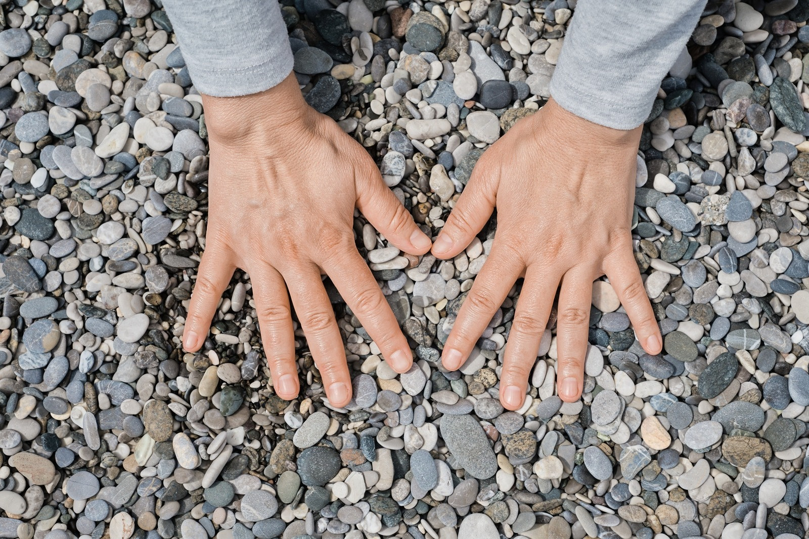 Close-up of two hands resting on smooth pebbles outdoors, illustrating grounding and awareness of physical sensations during EMDR therapy.