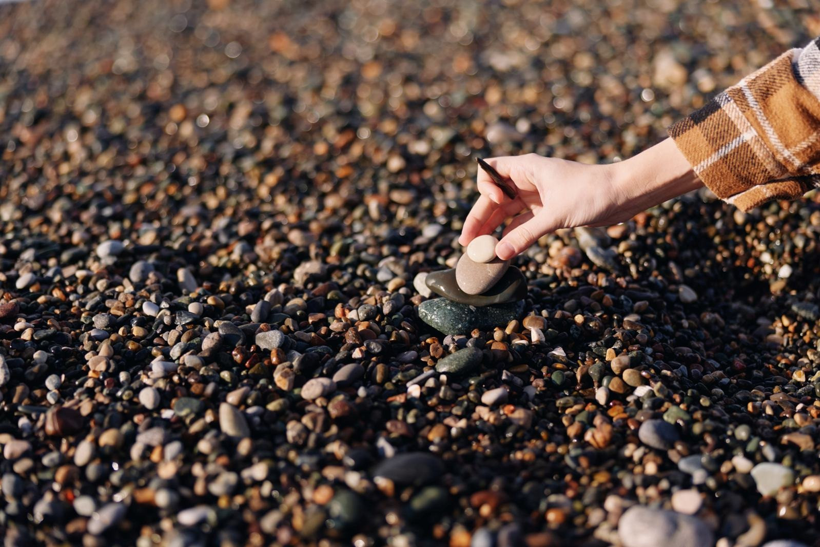 A hand carefully stacking smooth pebbles on a rocky beach, symbolizing calm, balance, and mindfulness.