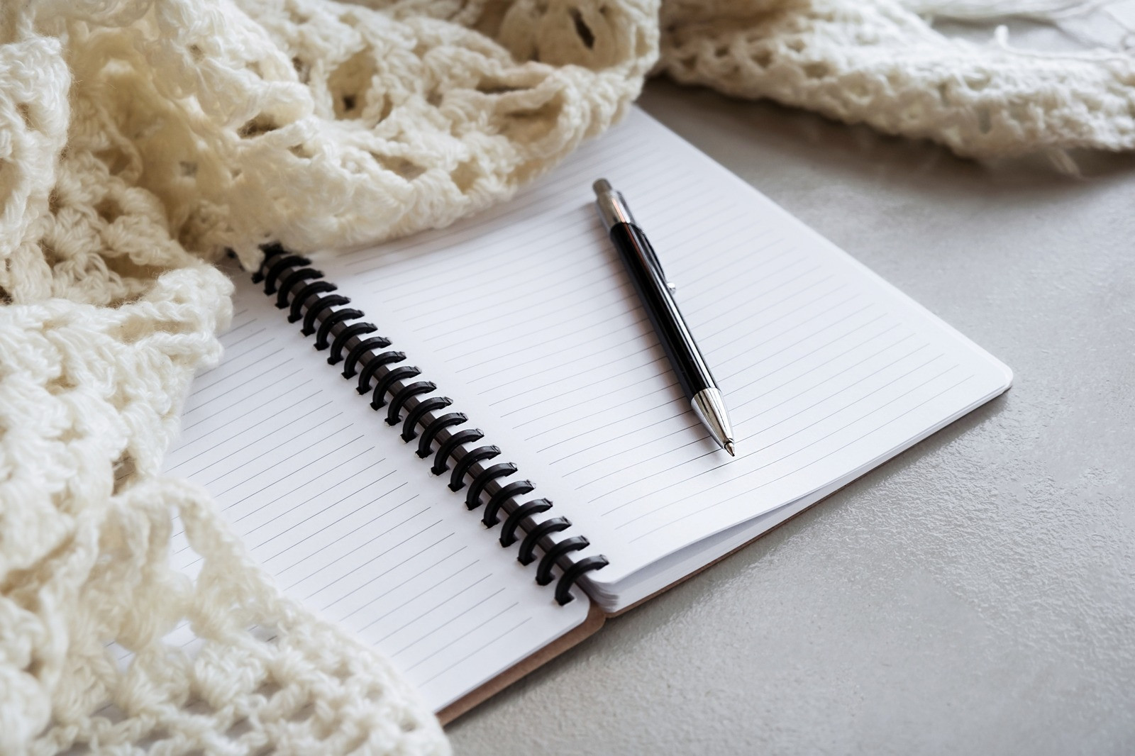 A black and silver pen resting on an open lined notebook beside a cream knitted blanket.
