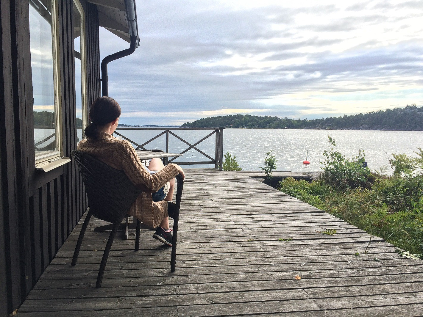 Person sitting quietly on a wooden deck overlooking a calm lake and distant trees.