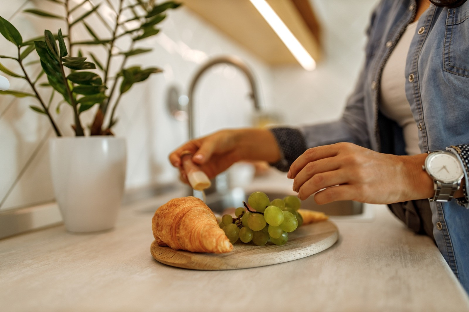 Person preparing a light meal with fruit and a croissant in a kitchen